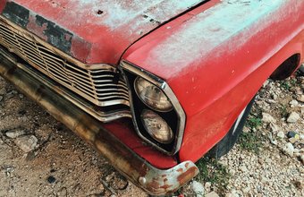 Detailaufnahme eines alten, verrosteten roten Autos mit verblasstem Lack und beschädigter Stoßstange.
