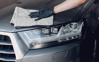 Person reinigt die Front eines Autos mit einem Mikrofasertuch.