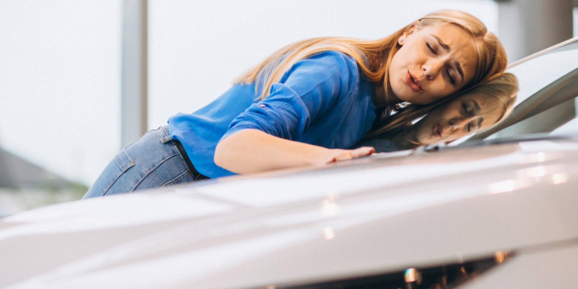 Junge Frau lehnt sich glücklich an ein Auto und streicht über die Motorhaube.