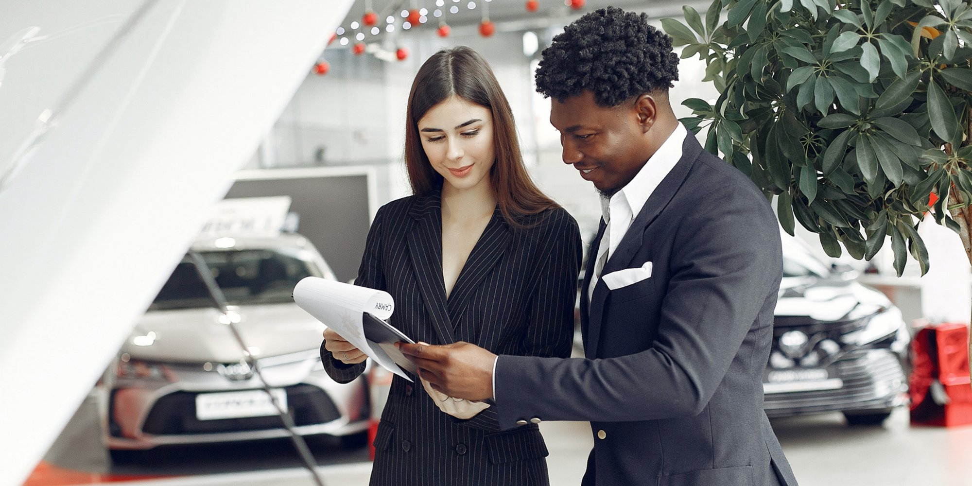 Zwei Personen im Autohaus besprechen gemeinsam ein Dokument, im Hintergrund stehen Fahrzeuge.